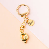 The-darling-effect Q Bubble Letter Keychain Bag Charm features a gold bubble letter Q, round clip, and small disc charm, displayed on a pastel pink and peach background.