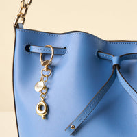 Close-up of a light blue leather handbag with a drawstring closure, featuring the-darling-effect's Q Bubble Letter Keychain Bag Charm attached to a grommet, showcasing its circular charm and decorative ring.