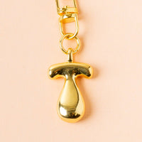 The T Bubble Letter Keychain Bag Charm by the-darling-effect features a gold T-shaped pendant on a matching chain, ideal as a personalized keychain or bag charm, shown against a pale peach background.