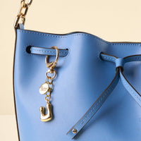 Close-up of a light blue leather handbag with black edges, featuring the-darling-effect's U Bubble Letter Keychain Bag Charm and round tag on a strap threaded through metal eyelets for a personalized, elegant touch.