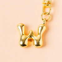 The-darling-effect W Bubble Letter Keychain Bag Charm features a shiny gold, bold rounded "W" pendant—perfect as a personalized accessory or bag charm, shown against a pale peach background.