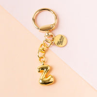 The Z Bubble Letter Keychain Bag Charm by the-darling-effect features a puffy golden Z charm and a small engraved disc—perfect as a personalized keychain or chic accessory for your bag.