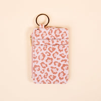 The Darling Effect's Born Wild Keychain Wallet, featuring a pink and light brown leopard print, gold zipper, two card slots, and a round keyring, is displayed on a beige background.