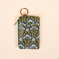 The Darling Effect’s Everbloom Forest Green Keychain Wallet features a white and light blue floral pattern, gold zipper, and keyring—a slim, functional wallet for floral lovers—shown on a neutral beige background.