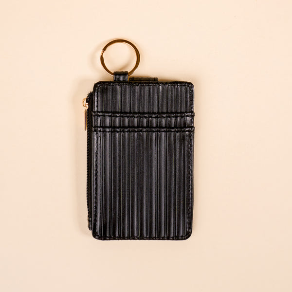 The Darling Effect's Black Ripple Ridge Keychain Wallet features vertical ripples, a gold keyring, multiple card slots, and a zippered pocket, shown on a beige background.
