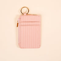 The Darling Effect’s Blush Ripple Ridge Keychain Wallet features vertical stitching, a side zipper, two card slots, and a gold keyring—ideal for slim wallet seekers—shown on a beige background.