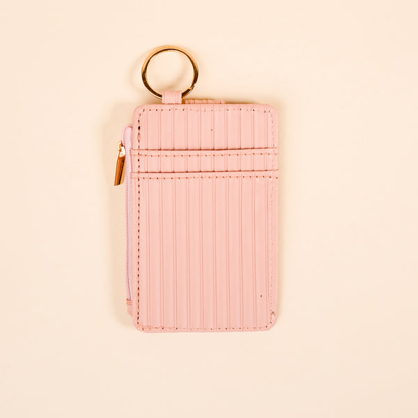 The Darling Effect’s Blush Ripple Ridge Keychain Wallet features vertical stitching, a side zipper, two card slots, and a gold keyring—ideal for slim wallet seekers—shown on a beige background.