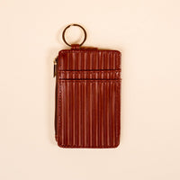 The Darling Effect's Cognac Ripple Ridge Keychain Wallet features brown, vertically-ribbed leather, a zipper pocket, and a gold key ring, shown on a plain beige background.
