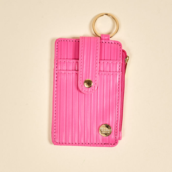 The Darling Effect Hot Pink Ripple Ridge Keychain Wallet features vertical stripes, a snap-button strap, gold key ring, and zippered coin holder, shown on a cream background.