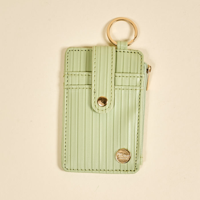 The Darling Effect Sage Ripple Ridge Keychain Wallet features a pastel green hue, vertical ribbed texture, gold snap and zipper, zippered coin holder, and multiple card slots for convenience.
