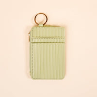 The Darling Effect's Sage Ripple Ridge Keychain Wallet—a small, light green wallet with card slots, zip coin holder, vertical stitching, and a gold keyring—displayed on a cream background.