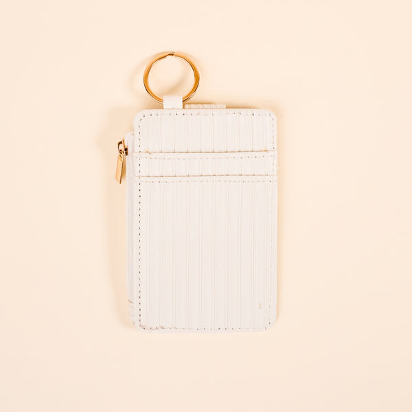 The Darling Effect’s White Ripple Ridge Keychain Wallet features vertical stitching, a zippered coin pocket, two card slots, and a gold key ring, shown on a light beige background.