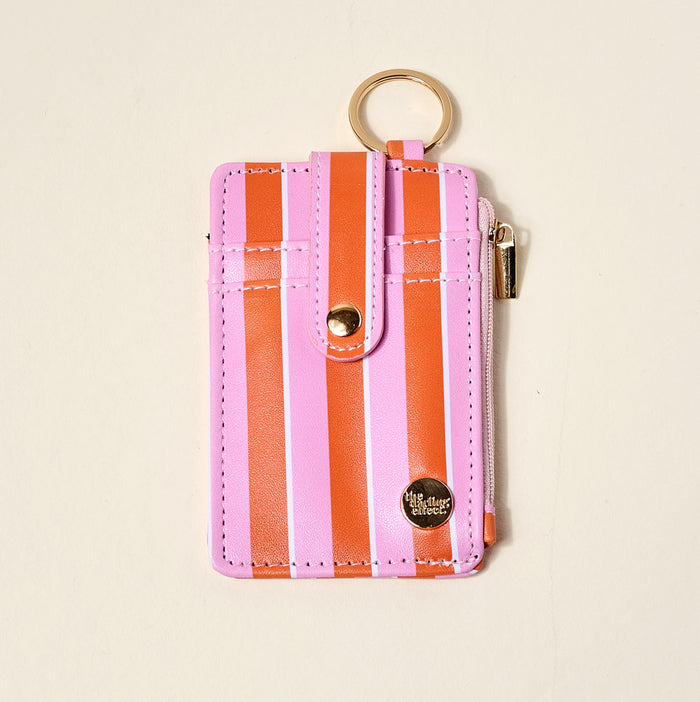 The Darling Effect Sicily Stripes Pink Keychain Wallet features pink and orange stripes, a gold keyring, snap button strap, zipper pocket, and a round metal emblem—combining style and function for everyday use.