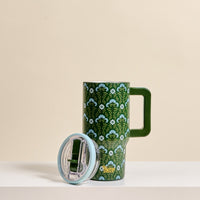 The Darling Effect Everbloom Forest Green 20 oz Lifestyle Flip Straw Tumbler features a white and blue floral pattern, large handle, insulated stainless steel body, and clear plastic lid with flip straw, shown on a white surface against a beige background.