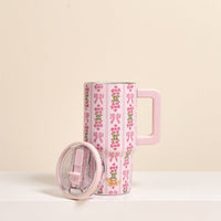 The Oh So Fancy Pink 20 oz Lifestyle Flip Straw Tumbler by the-darling-effect, featuring a pink handle, lid, bow and flower designs, stands on a white surface with its clear lid beside it against a beige background.