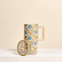The Darling Effect Poppin' Petals Aqua 20 oz Lifestyle Flip Straw Tumbler features a tall beige insulated stainless steel body, blue floral pattern, beige handle, and includes a clear lid with green rim.