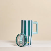 The Darling Effect Sicily Stripes Teal 20 oz Lifestyle Flip Straw Tumbler features vertical green and white stripes, a large light blue handle, and a matching lid, displayed on a light surface with a beige background.