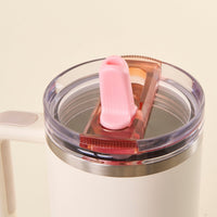 A close-up of the-darling-effect Pink 40 oz Lifestyle Flip Straw Lid shows a white insulated travel mug with a leak-resistant Flip Straw Lid, pink flip-top spout cover, handy handle, and metallic rim against a soft beige background.