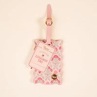 The Darling Effect's Everbloom Dusty Rose Jetsetter Luggage Tag features a pink scalloped edge, floral pattern, gold buckle, privacy flap, and label. This chic accessory is displayed on a plain light background.