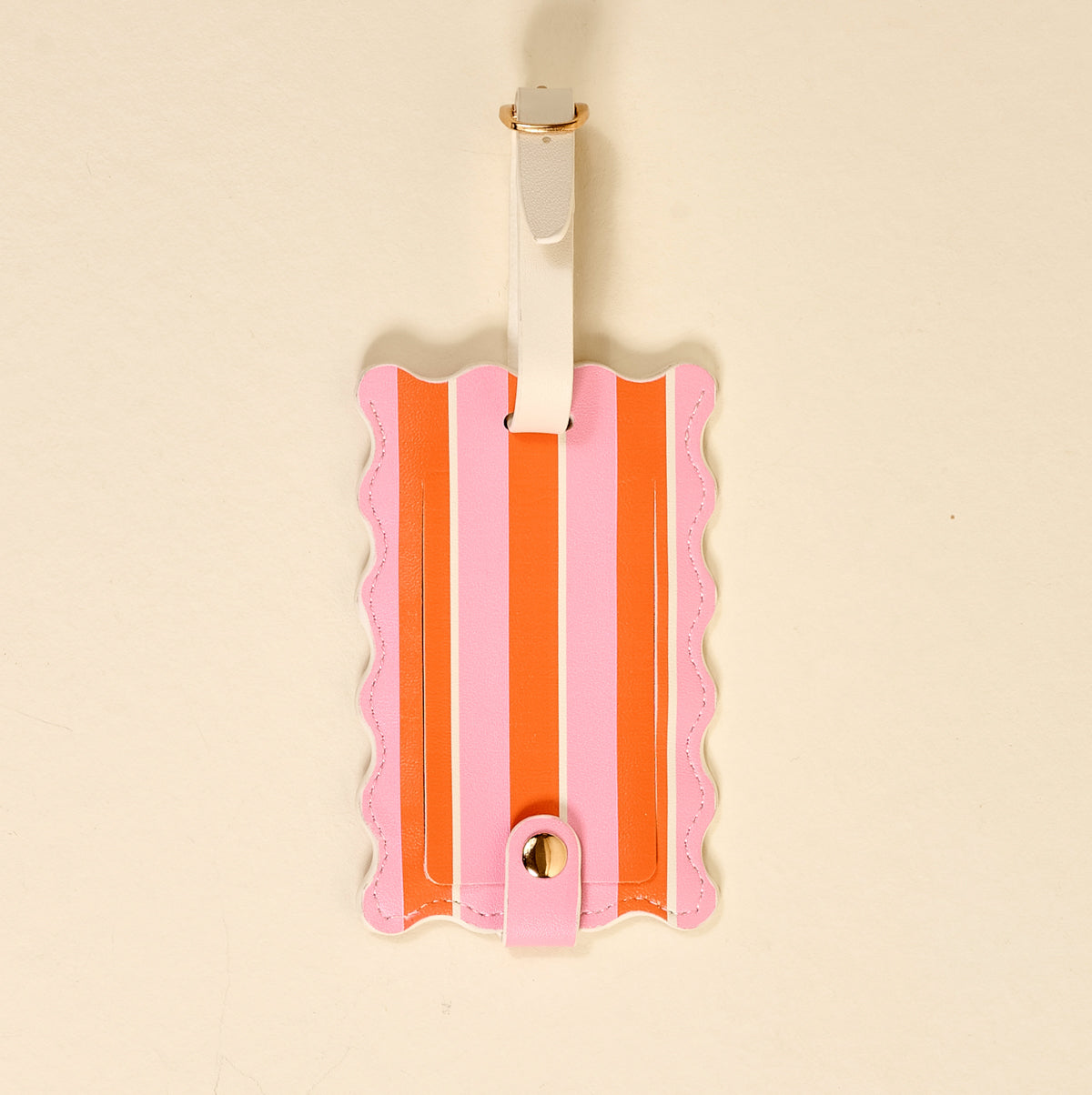 The Darling Effect’s Sicily Stripes Pink Jetsetter Luggage Tag showcases orange stripes, scalloped edges, and a white strap with a gold buckle, pictured on a plain beige backdrop.