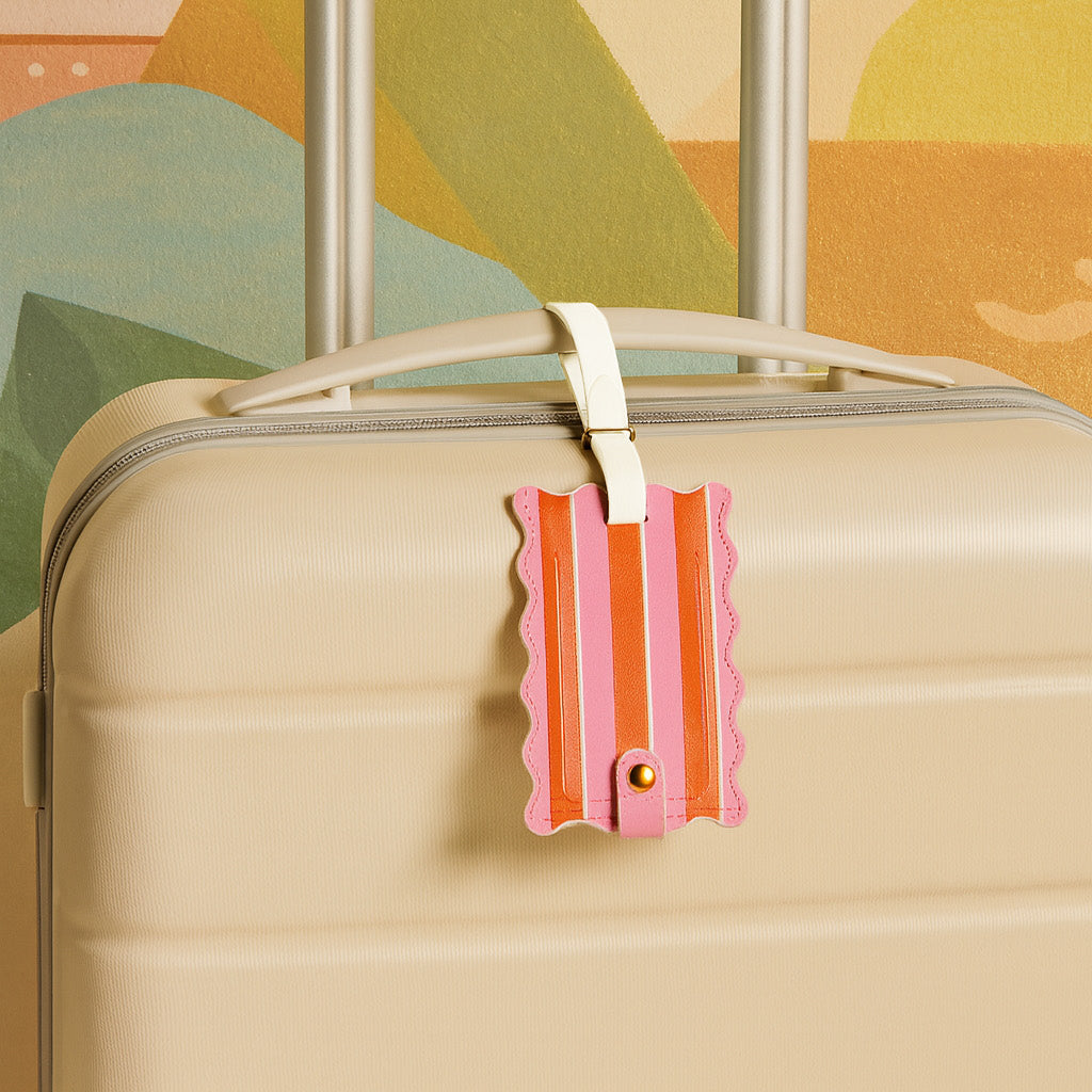A beige hard-shell suitcase with a white handle features The Darling Effect's Sicily Stripes Pink Jetsetter Luggage Tag and a privacy flap, set against an abstract background with green and orange shapes.