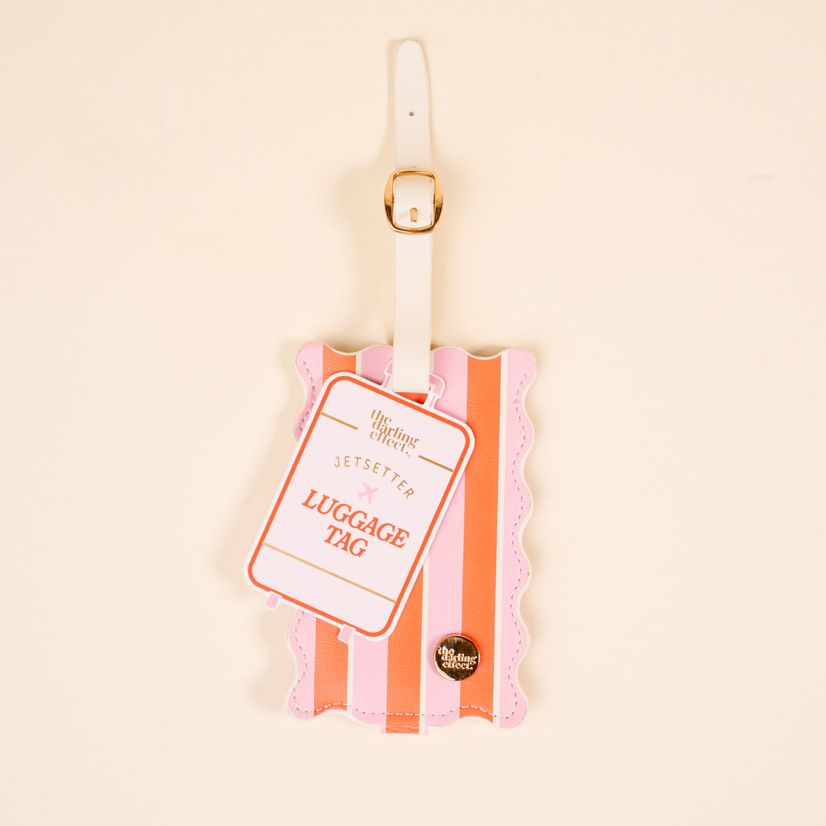 The Darling Effect's Sicily Stripes Pink Jetsetter Luggage Tag features pink and orange stripes, wavy edges, a white strap with a gold buckle, and "JETSETTER LUGGAGE TAG" on the front, shown on a beige background.
