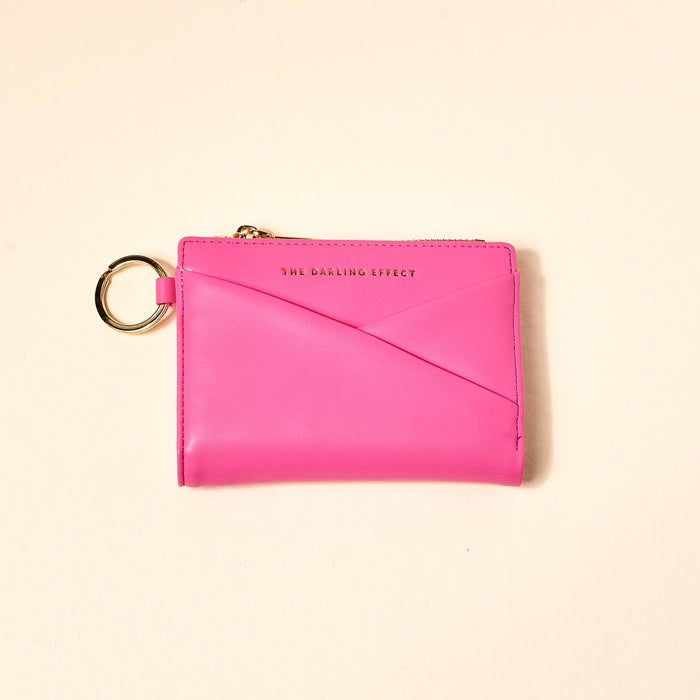 The Darling Effect’s Hot Pink Luxe Pocket Wallet is a vegan leather wallet with gold zipper and keyring, featuring “THE DARLING EFFECT” in gold on the front—an everyday essential shown against a light beige background.