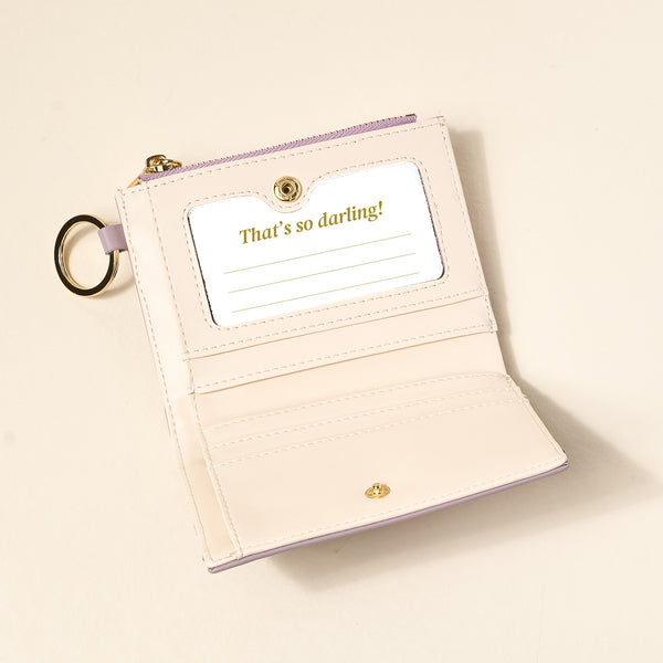 The Darling Effect’s Lavender Luxe Pocket Wallet, crafted from light vegan leather with a gold ring and snap, opens to reveal a card slot holding a card that says 'That's so darling!' in gold text, plus extra space for notes.