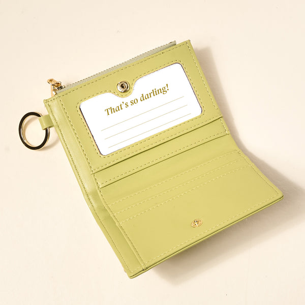 The Darling Effect’s Poppin' Petals Aqua Luxe Pocket Wallet is a light green vegan leather wallet with card slots, a zippered coin pocket, a gold key ring, and a “That’s so darling!” card. Shown open on a beige background.