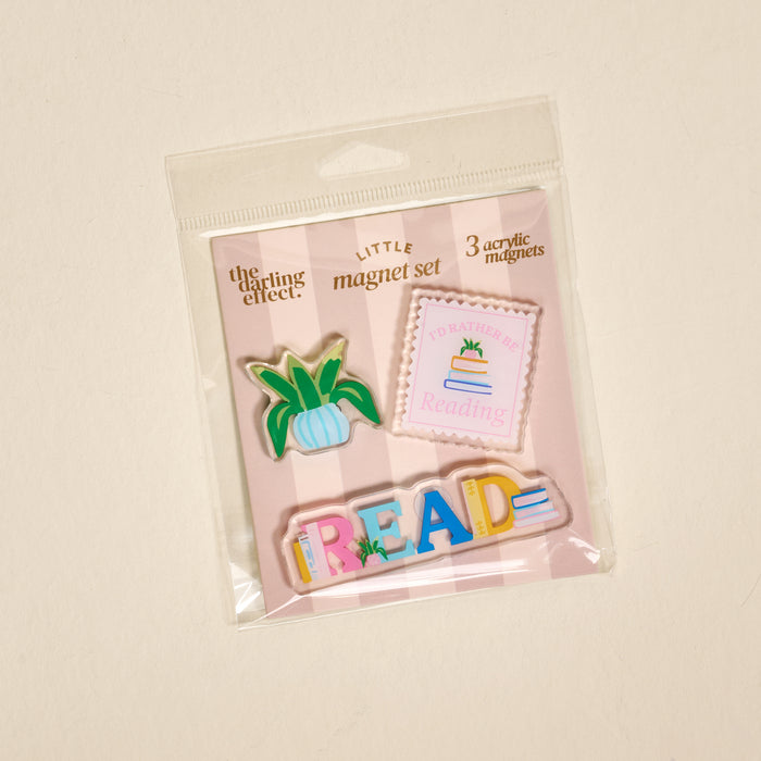 Introducing the All Booked Up Little Magnet Set by The Darling Effect—a set of three vibrant acrylic magnets packaged together, featuring a potted plant, a book-themed square with text, and bold READ lettering. Perfect for decorating your space or adding flair to your fridge!.