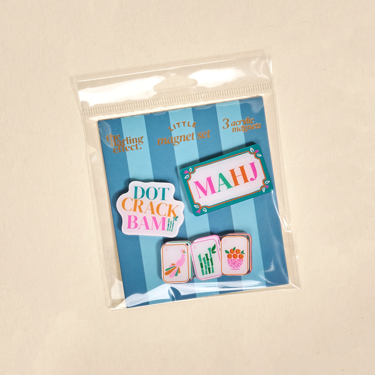 Introducing the Let’s Play Mahjong Little Magnet Set by The Darling Effect: a package of three acrylic fridge magnets, each featuring a beautifully illustrated Mahjong tile—labeled DOT, CRACK, and BAM—set against a blue background and packaged in a clear plastic bag. These charming magnets make the perfect decorative accents for your kitchen.