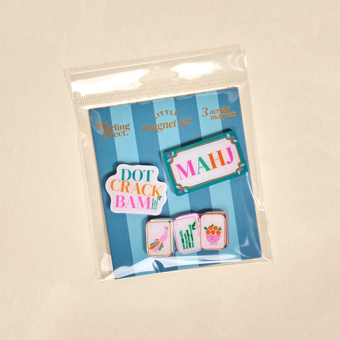 Introducing the Let’s Play Mahjong Little Magnet Set by The Darling Effect: a package of three acrylic fridge magnets, each featuring a beautifully illustrated Mahjong tile—labeled DOT, CRACK, and BAM—set against a blue background and packaged in a clear plastic bag. These charming magnets make the perfect decorative accents for your kitchen.