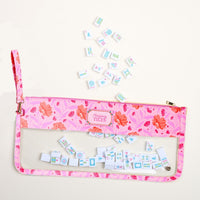 The Darling Effect's Poppin' Petals Hot Pink Mahjong Tile Keeper Pouch, featuring a transparent section, holds small Mahjong tiles—some scattered on a light surface above the stylish organizer.