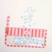 The Darling Effect's Sicily Stripes Pink Mahjong Tile Keeper Pouch, featuring pink and orange stripes, neatly stores small Mahjong tiles, with a few vibrantly scattered outside the organizer on a light surface.