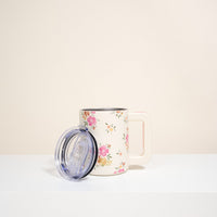 The Darling Effect's Endless Daydream Cream 14 oz Insulated Mug features a floral pattern with pink and orange flowers, green leaves, a light pink handle, double-wall insulation, and comes with a clear lid placed next to it.