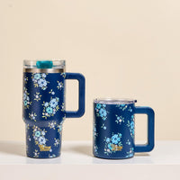 Two Endless Daydream Navy 14 oz Insulated Mugs by The Darling Effect, featuring handles, clear lids, and light blue floral patterns, sit side by side on a white surface—perfect for keeping your coffee hot with double-wall insulation.