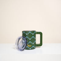 The Darling Effect Everbloom Forest Green 14 oz Insulated Mug, with a floral design, double-wall insulation, large handle, and transparent plastic lid beside it, sits on a white surface against a plain light background.