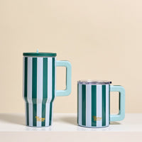 Two Sicily Stripes Teal 14 oz Insulated Mugs by The Darling Effect, featuring green and white stripes with light blue handles and stylish double-wall insulation, sit on a white shelf against a pale yellow background.