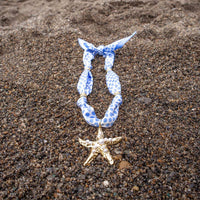 The Darling Effect Shore Thing Make a Statement Scarf Necklace, featuring blue and white polka dots and a gold starfish charm, is displayed on brown sand.