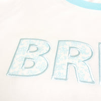 Close-up of light blue "BR" letters with a floral pattern, embroidered on The Darling Effect's Bride Oversized Crew. The soft white fabric and light blue trimmed collar make this sweatshirt cozy and stylish.