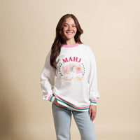 A woman with long brown hair smiles in The Darling Effect’s Mahjong Social Club Oversized Crew, featuring “MAHJ Snack Club” and illustrated mahjong tiles. She stands against a beige background—perfect for any cozy wardrobe.