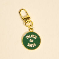 The Darling Effect's Too Cute for Rules Pawfect Collar Charm features a gold keychain with a green tag that says "TOO CUTE for RULES" in white, perfect for adding playful style to your pet’s collar accessories.