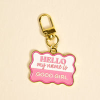 The Darling Effect Good Girl Pawfect Collar Charm is a gold keychain with a wavy pink and white tag that says "HELLO my name is GOOD GIRL"—a fun accessory to add playful style to your pet's collar or charm collection.