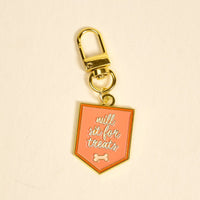 The Darling Effect’s Will Sit for Treats Pawfect Collar Charm features a gold keychain with a pink shield tag, white script, and bone icon—perfect for adding playful style to your pet accessories collection.