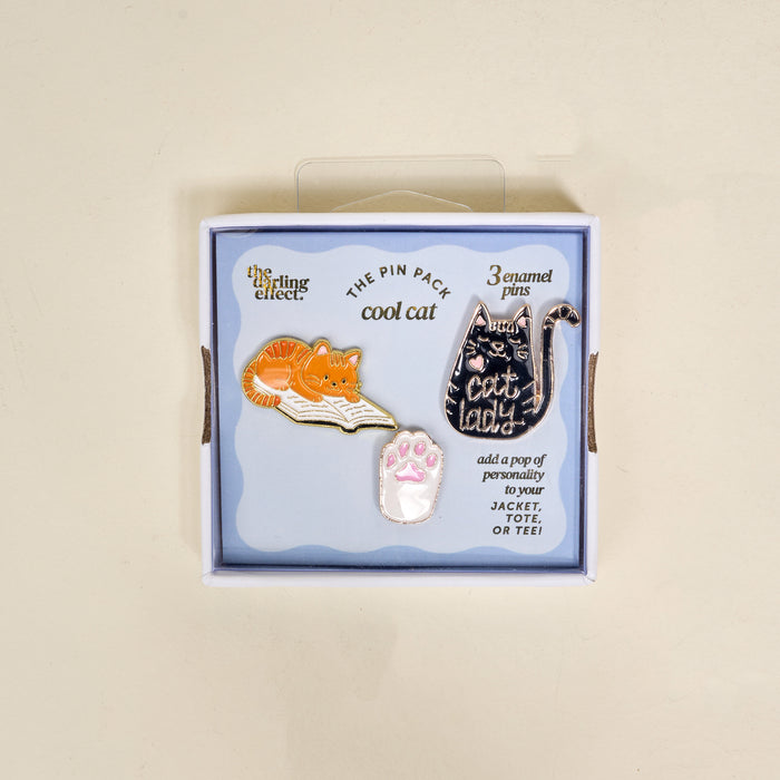 Cool Cat The Pin Pack by The Darling Effect features three cat-themed enamel pins—an orange cat on a book, a pink cat paw, and a black “cat lady” pin—in a blue box labeled “cool cat.” Add personality to your jacket, tote, or tee!.