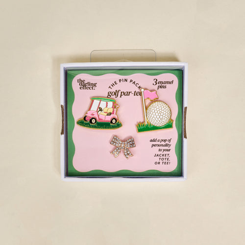 The Darling Effect’s Golf Par-Tee The Pin Pack features three pins—a pink golf cart, a golf ball by a pink flag, and a sparkling bow—in boxed “golf par-tee” packaging. Perfect for accessorizing jackets, totes, or tees.