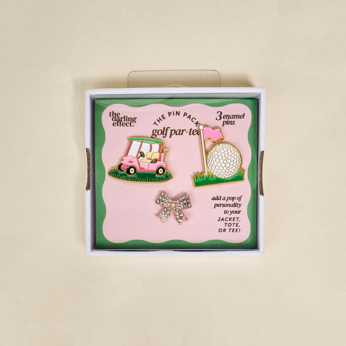 The Darling Effect’s Golf Par-Tee The Pin Pack features three pins—a pink golf cart, a golf ball by a pink flag, and a sparkling bow—in boxed “golf par-tee” packaging. Perfect for accessorizing jackets, totes, or tees.
