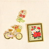 Petal Power The Pin Pack by The Darling Effect features three collectible pins: white and red flowers, a pink bike with floral basket, and a 50th ANNIVERSARY USA postage stamp—perfect for accessories lovers.