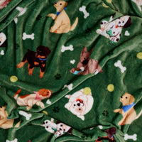 The Darling Effect’s Dog Days Snuggle Up Plush Blanket features green fleece playfully decorated with cartoon dogs, white bones, yellow balls, and green paw prints for a cozy and fun throw.