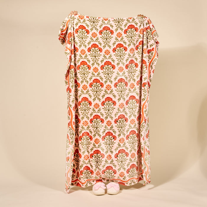 Someone holds up The Darling Effect’s Everbloom Dusty Rose Snuggle Up Plush Blanket, featuring a light pink background with an orange and green floral pattern, evoking the comfort of a cozy embrace.